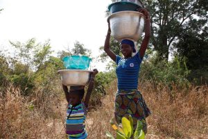 A woman carrying water containers on a rural track